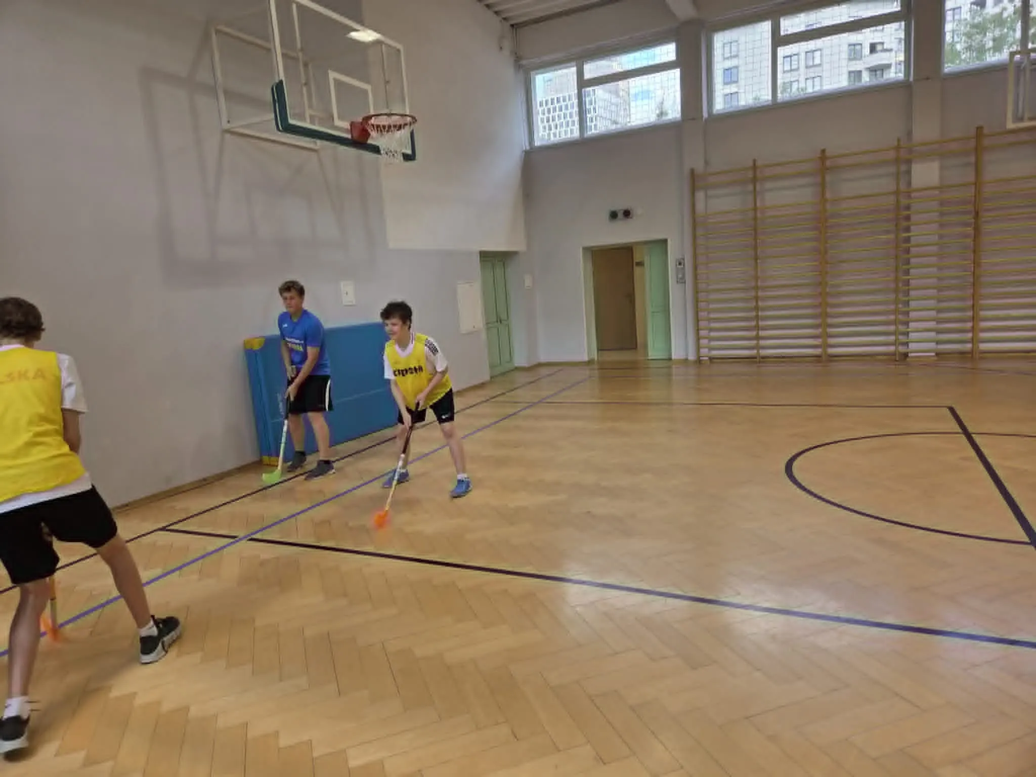 Zawodnicy przygotowują akcję ofensywną podczas szkolnego meczu unihokeja na sali gimnastycznej.