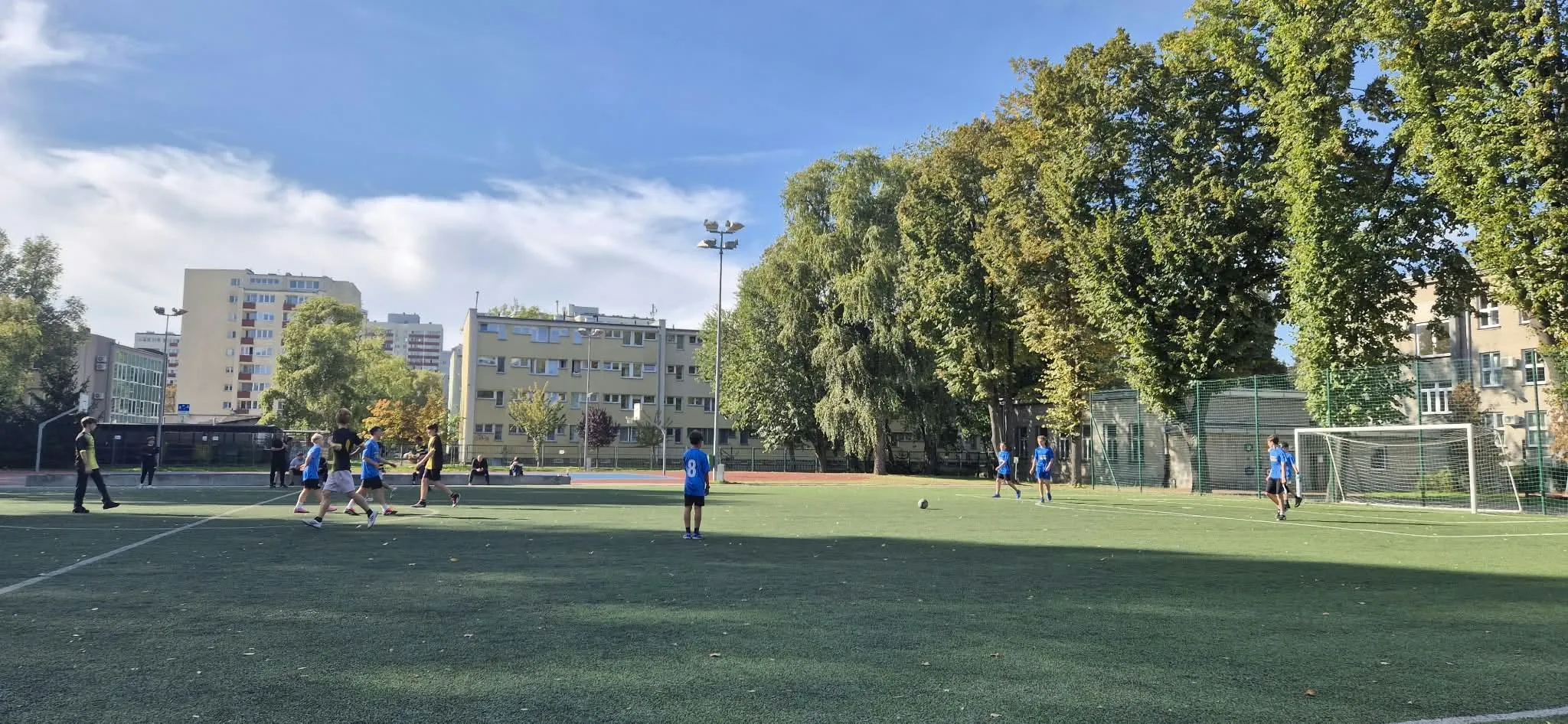 Uczniowie podczas szkolnego meczu piłki nożnej. Zawodnicy rywalizują o piłkę na boisku, rozwijając sprawność fizyczną i umiejętność współpracy w zespole.