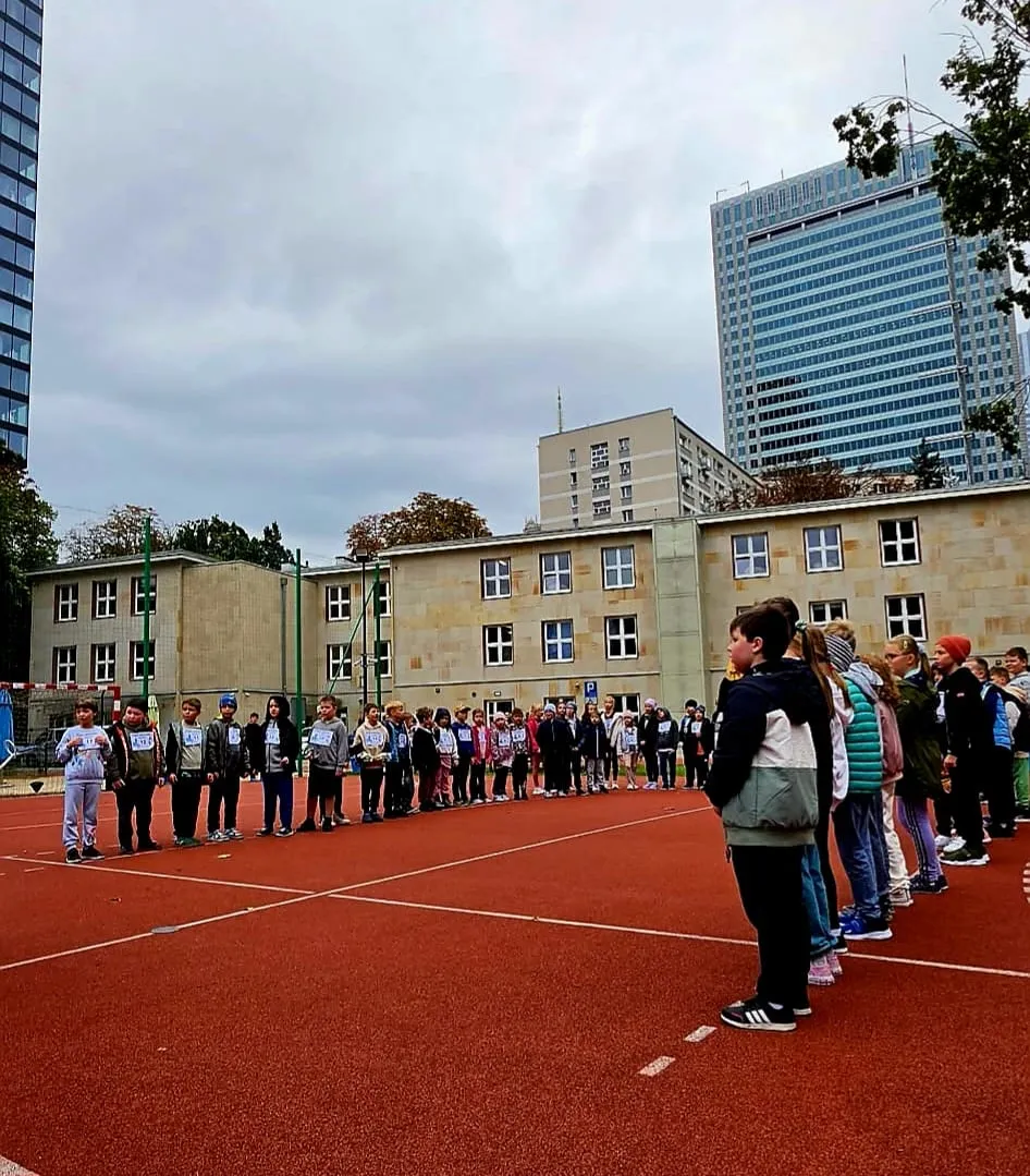 Uczniowie klas 1–3 zgromadzeni na szkolnym boisku przed rozpoczęciem zawodów lekkoatletycznych.