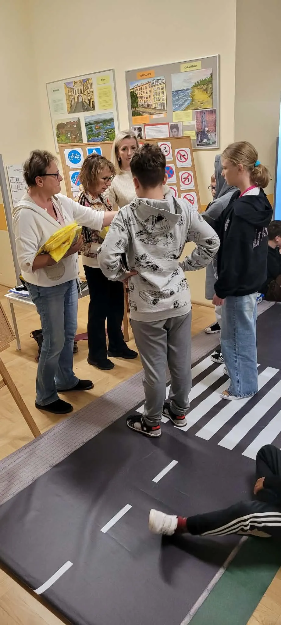 Uczniowie stoją przy przygotowanym przejściu dla pieszych podczas praktycznej nauki zasad bezpiecznego poruszania się po drodze.