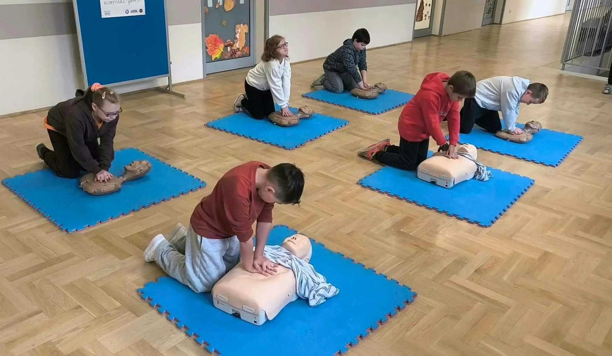 Uczniowie pochylają się nad fantomami i ćwiczą wykonywanie oddechów ratowniczych podczas zajęć z pierwszej pomocy.